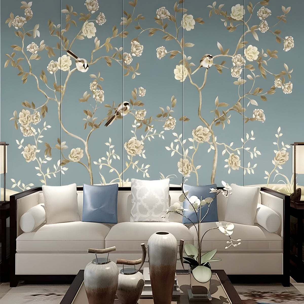 Papier peint panoramique fleuri bleu avec branches dorées et oiseaux derrière un canapé crème
